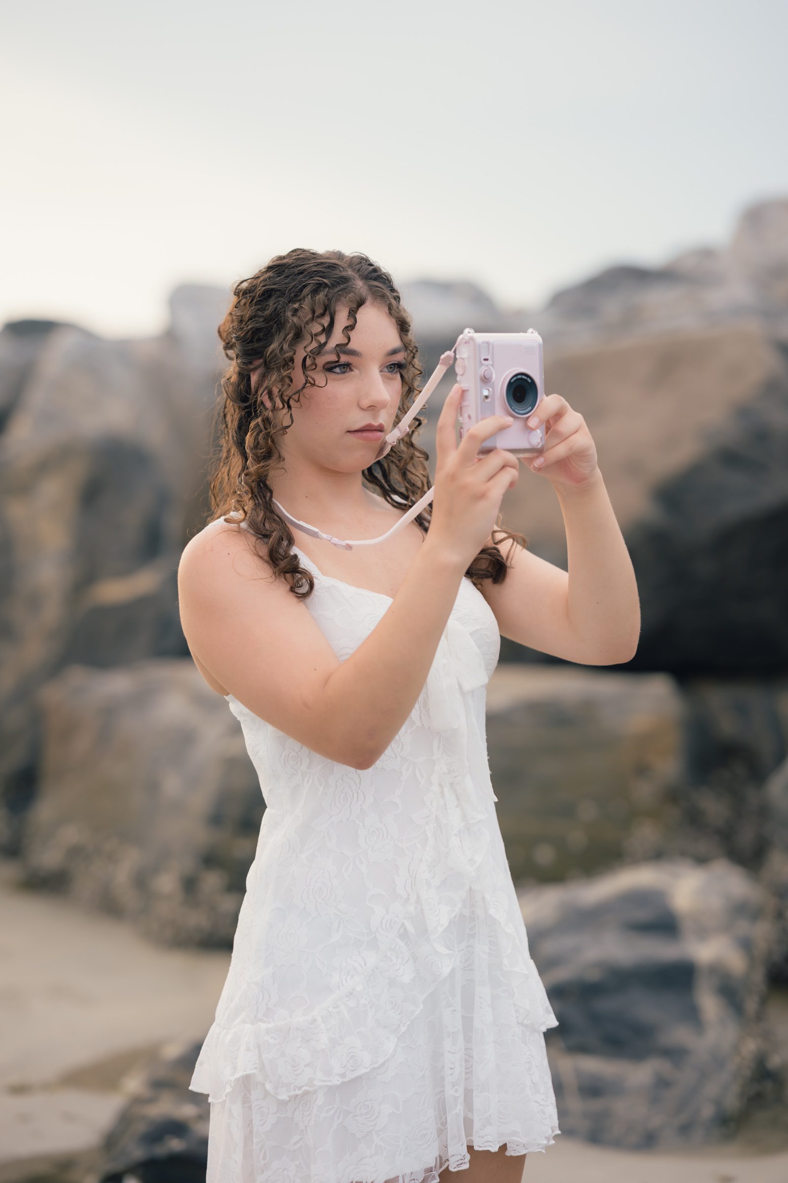 Senior looking at a pink instant camera beside the jetty rocks