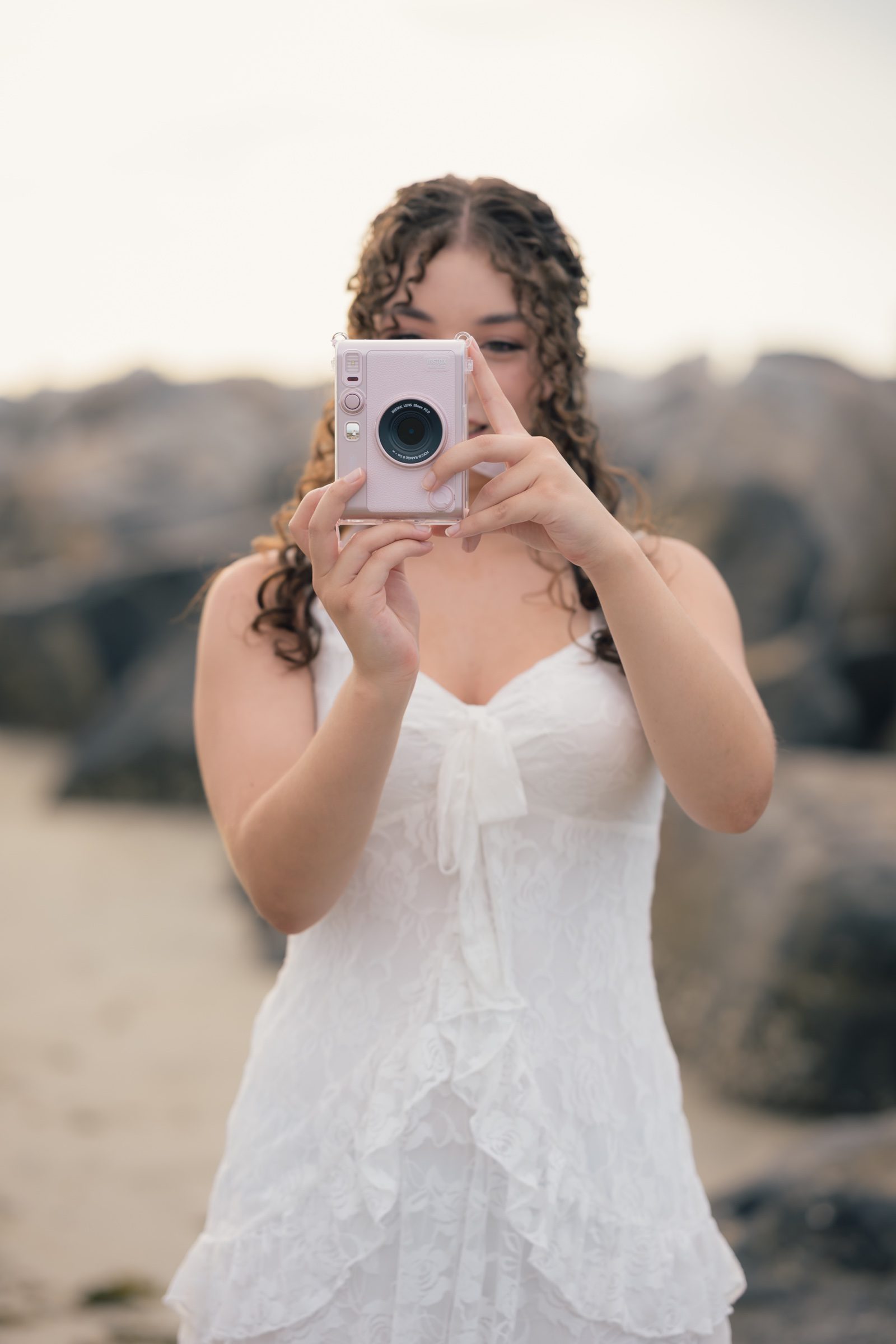 Senior holding a pink instant camera toward the photographer