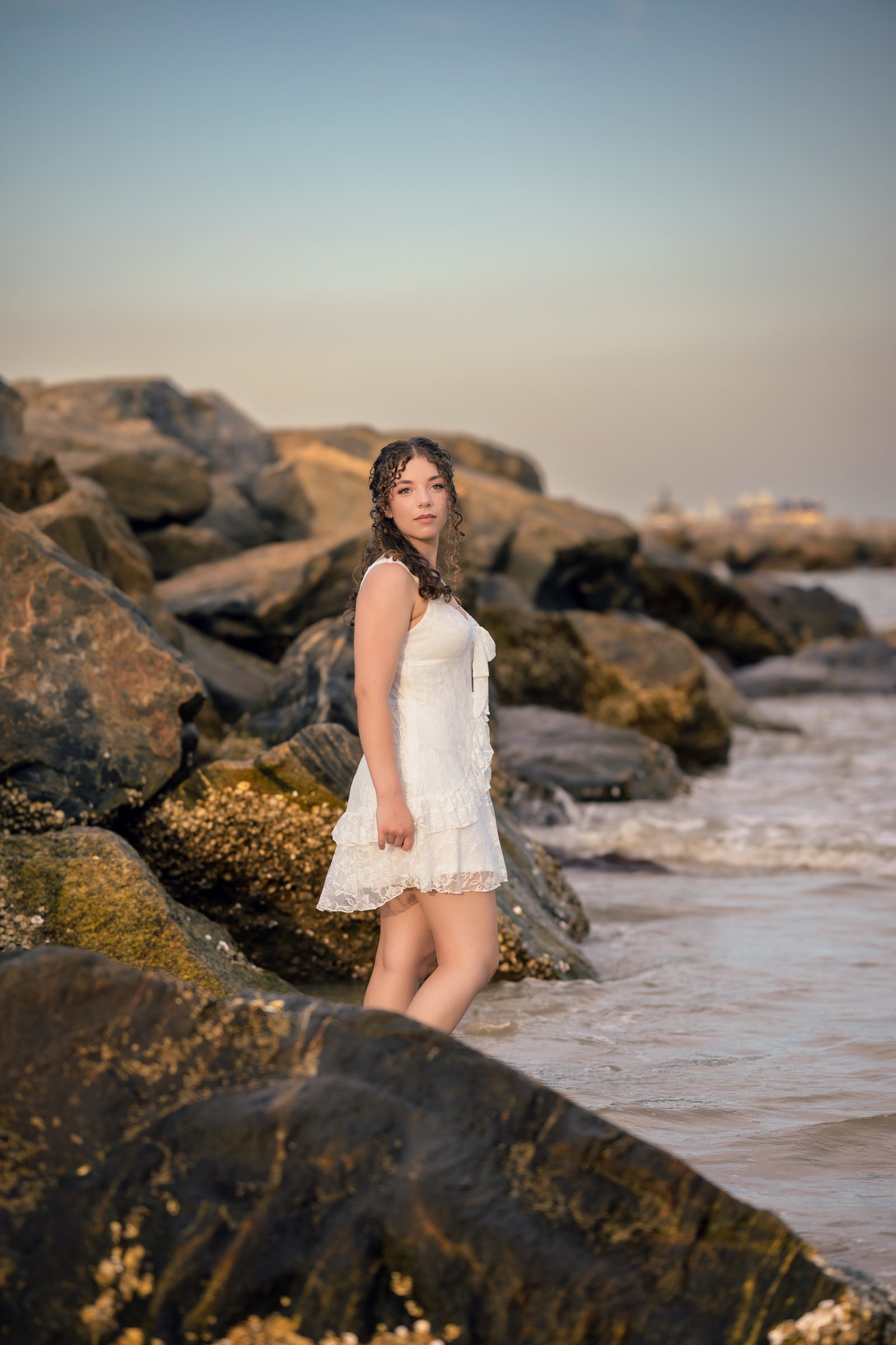 Senior in a white dress beside the jetty rocks near Cocoa Beach, Florida