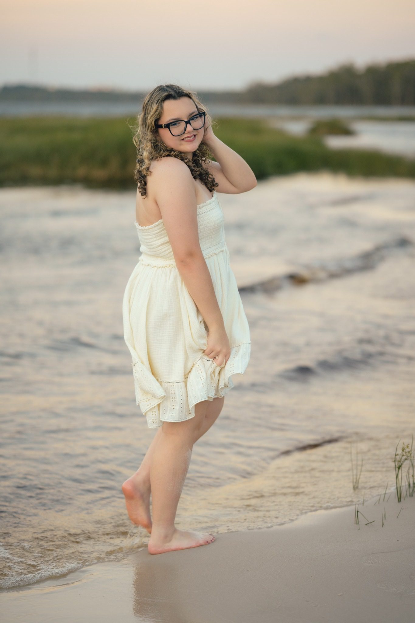 Senior in a white dress at the water’s edge during Clermont senior pictures