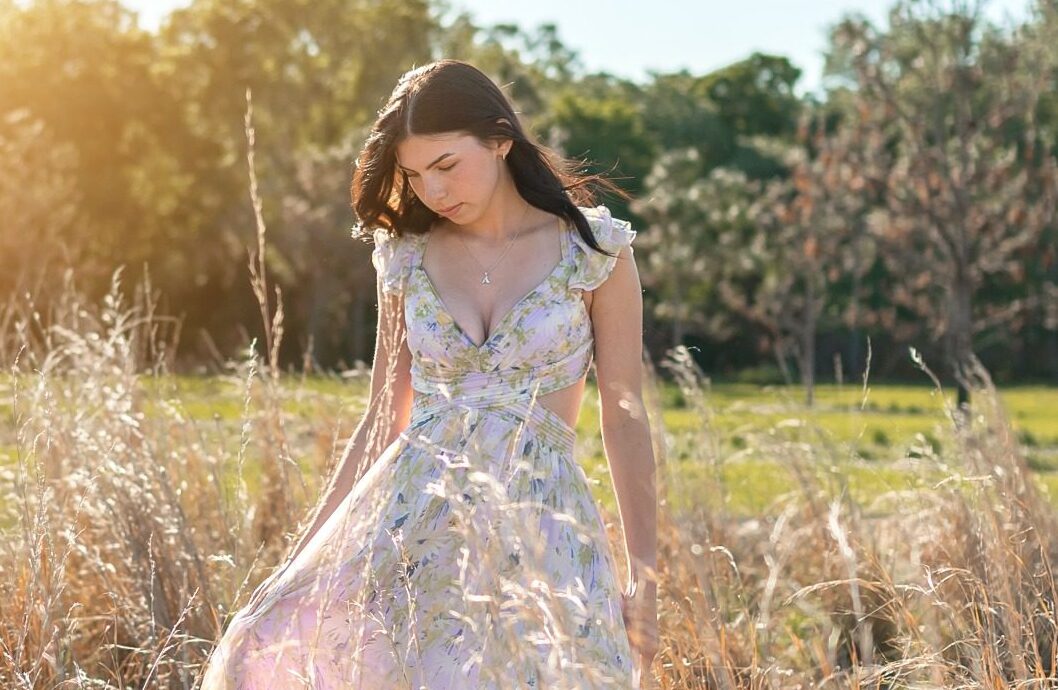 Senior in a floral dress walking through sunlit grass at Lake Louisa State Park in Clermont