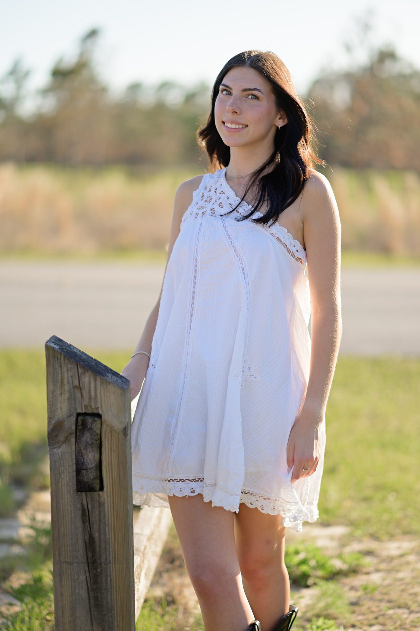 Senior portrait in a white dress beside a rustic fence at Lake Louisa State Park