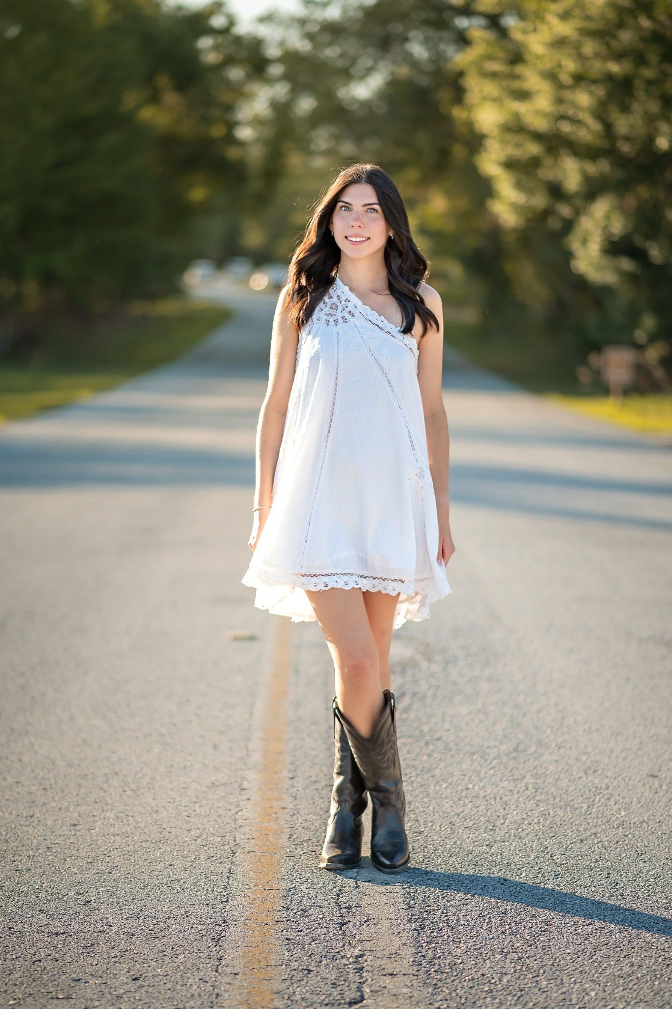 Senior standing on a tree-lined road in a white dress at Lake Louisa State Park