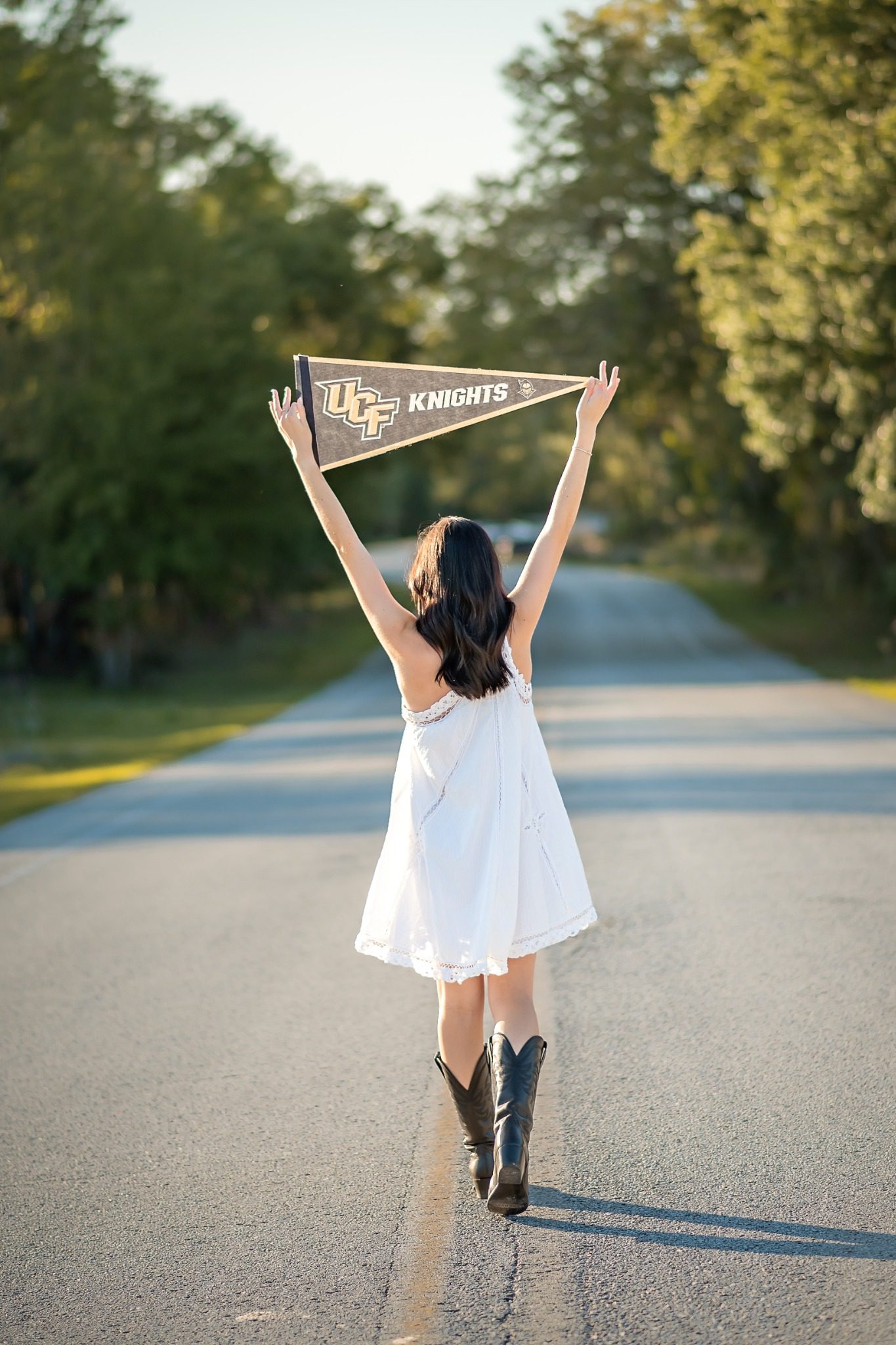 Senior raising a UCF pennant overhead on a tree-lined road at Lake Louisa