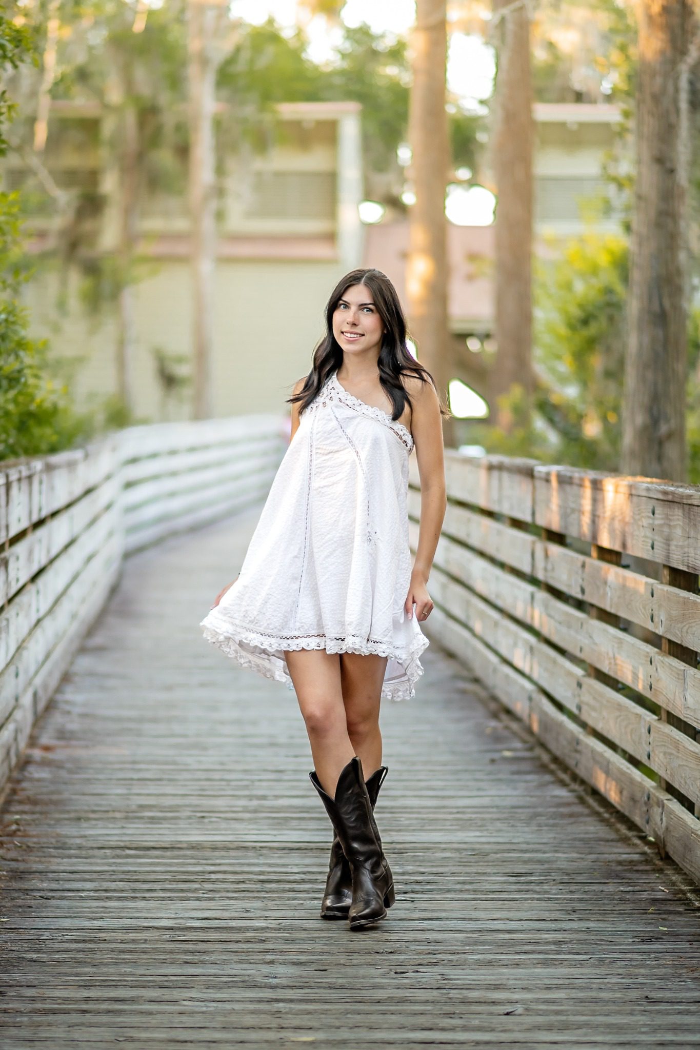 Senior in a white dress and black boots standing on a wooden boardwalk at Lake Louisa
