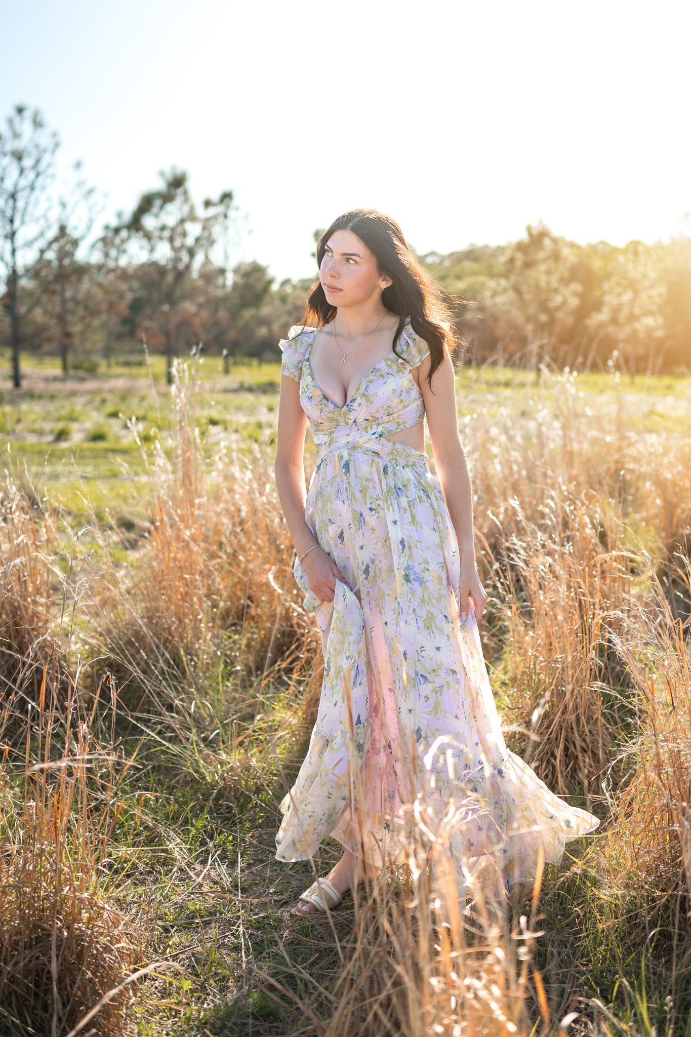 Full-length senior portrait in a floral dress beside tall grasses at Lake Louisa