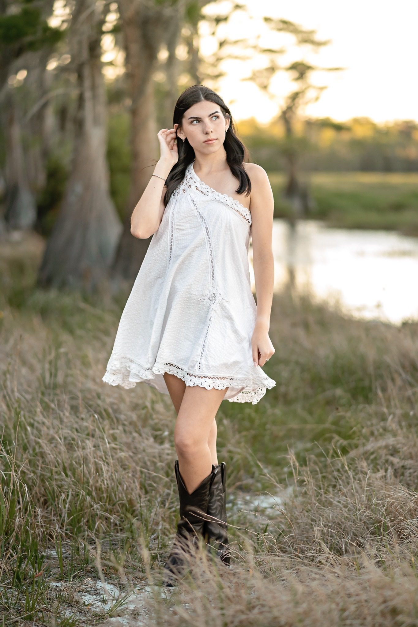 Senior in a white dress beside the lake under trees at Lake Louisa