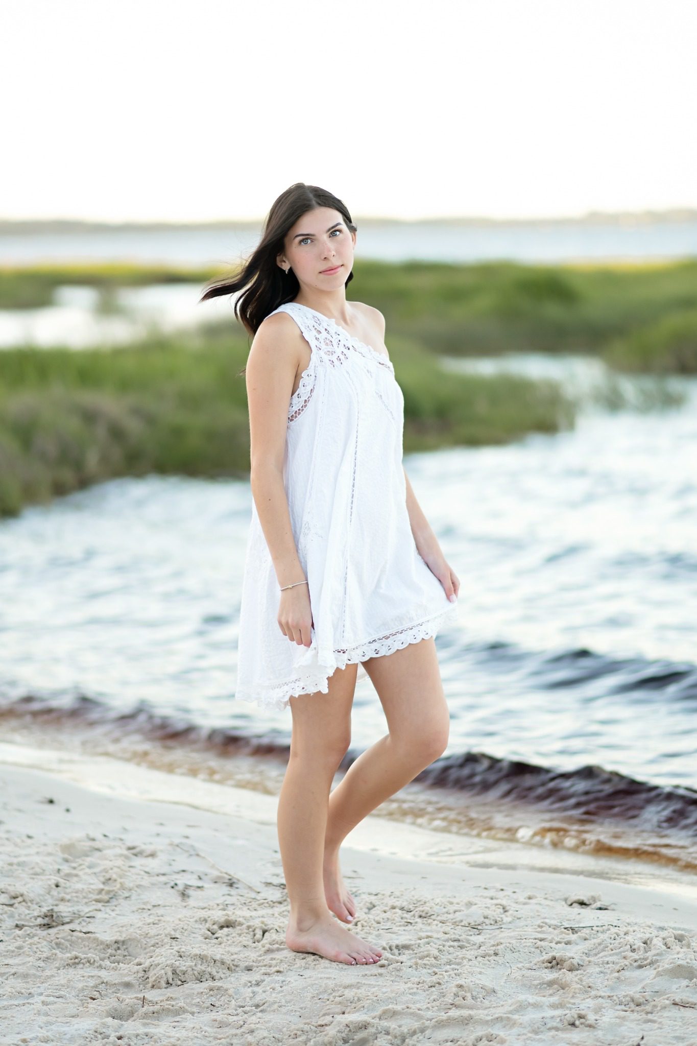 Senior in a white dress walking barefoot on the sandy Lake Louisa shoreline