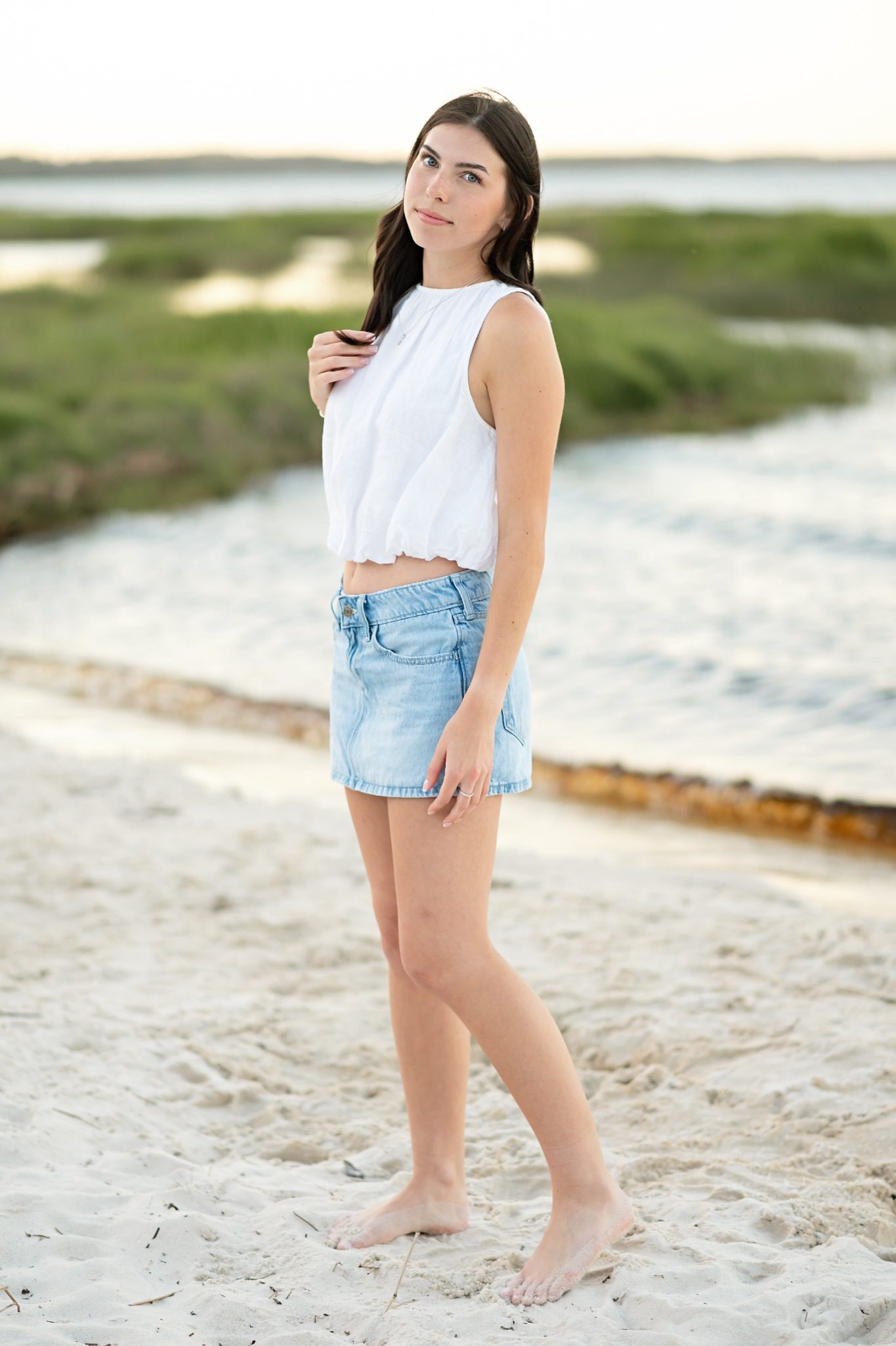 Senior looking over her shoulder in a denim skirt on the Lake Louisa shoreline