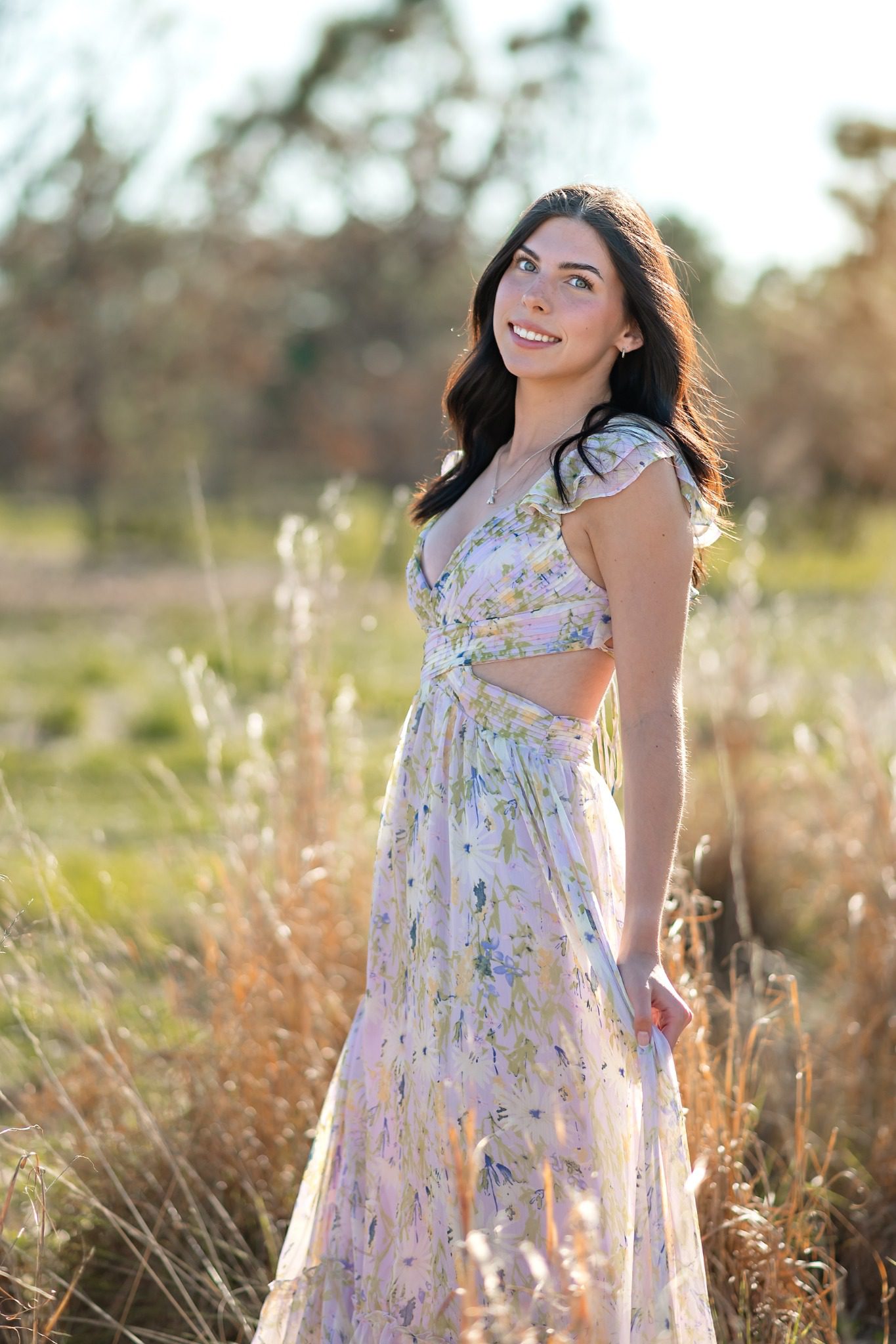 Smiling senior in a floral dress with wildflowers and trees at Lake Louisa State Park