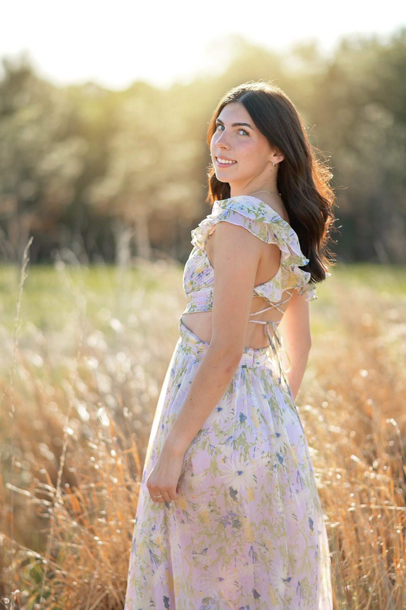 Senior looking over her shoulder in a floral dress in a Lake Louisa field